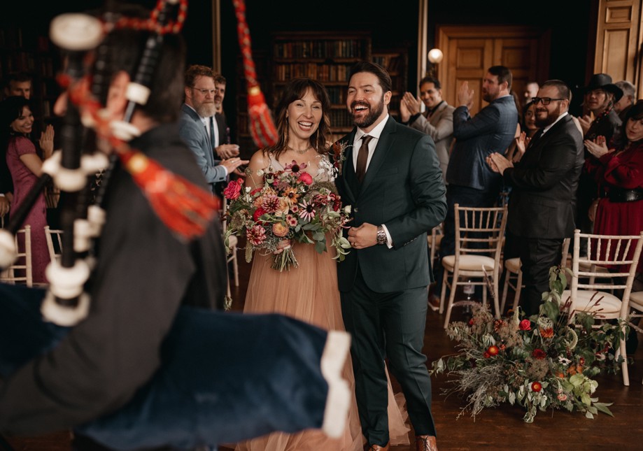 At a wedding in Cambo House, bride carries a natural bouquet of autumnal flowers with lush greenery.  Floral arrangements on the floor enhance the elegant, garden-inspired atmosphere.